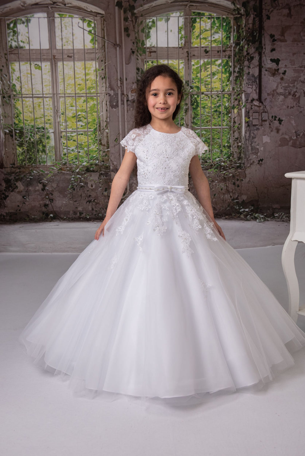 Elegant short sleeve Communion dress, features a lace with sequence and beaded pearls on bodice, scoop neckline, embellished beaded pearls waist, statin and tulle skirt.  Sizes: 10.5 to 14.5